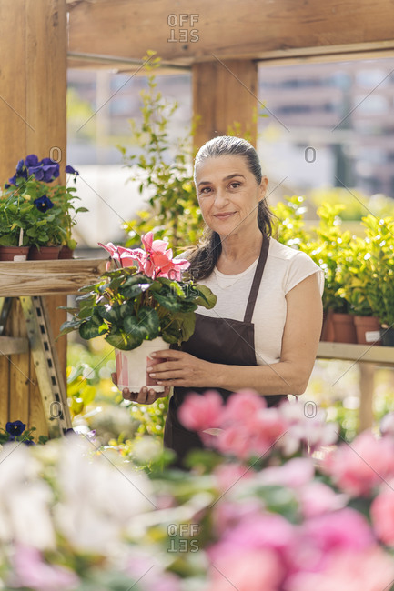 Beautiful middle aged woman working in plant nursery smiling and looking at camera.