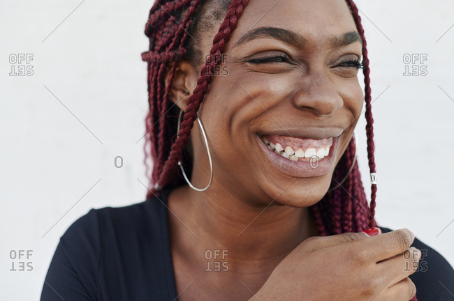 Carefree young African woman with colorful braided hair laughing while standing in front of a brick wall