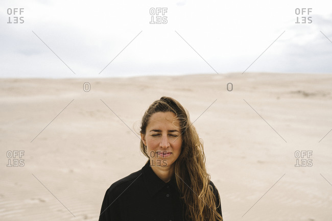 Woman with eyes closed, sand dunes on background