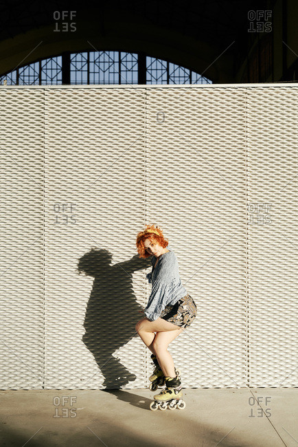 Young alternative redhead girl with roller skates in a metal wall
