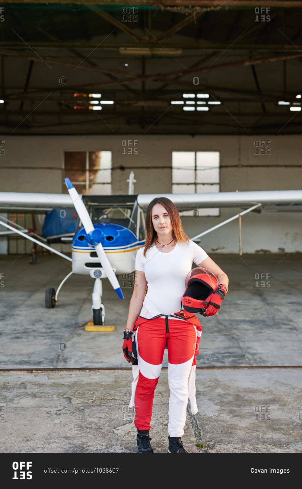 Young female skydiver in a plane hangar with a plane behind her