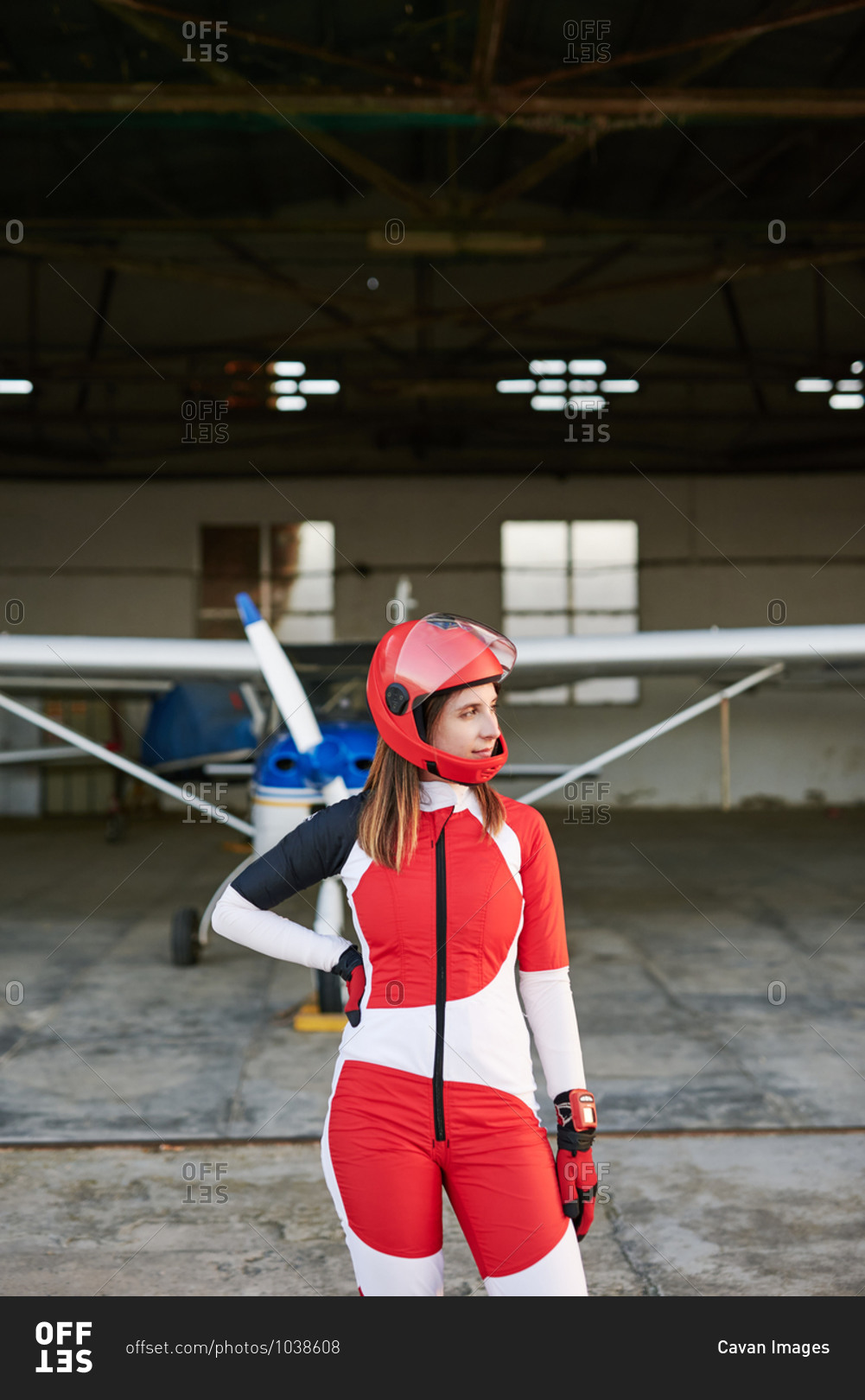 Young female skydiver in a plane hangar with a plane behind her