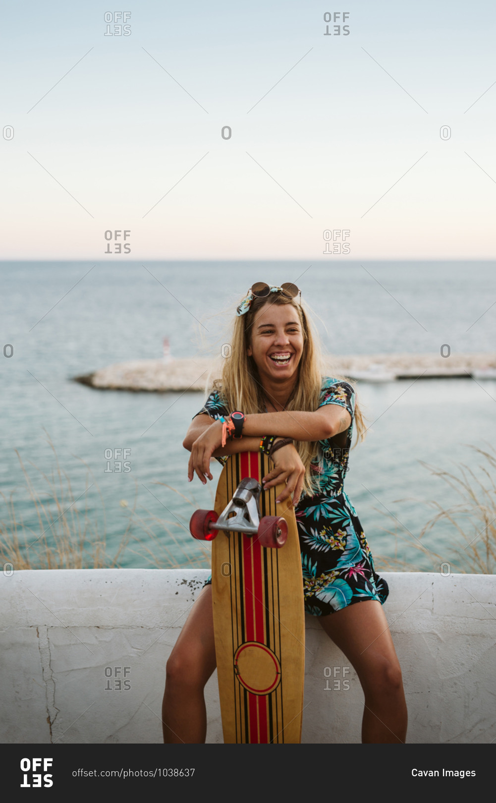 Laughing female with long board skate in front of Mediterranean sea