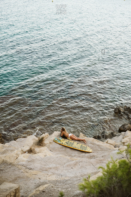 Female surfer laying down with orange surfboard at Moraira's small bay