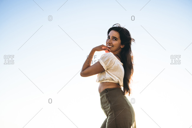 Young Latina Woman smiling by the ocean at golden hour in summertime