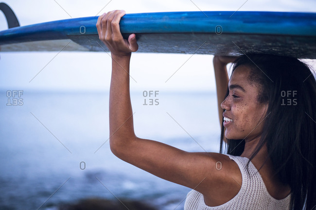 Black Multiracial Woman lifestyle portrait by the ocean with surfboard