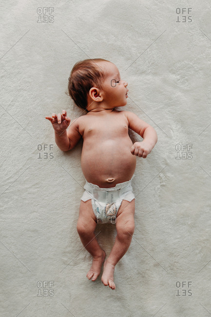 Newborn baby in only a diaper laying on white blanket