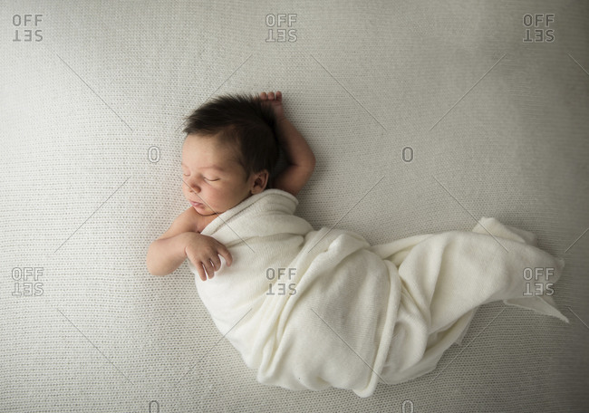 Candid Newborn Baby With Long Hair Sleeps in White Swaddle