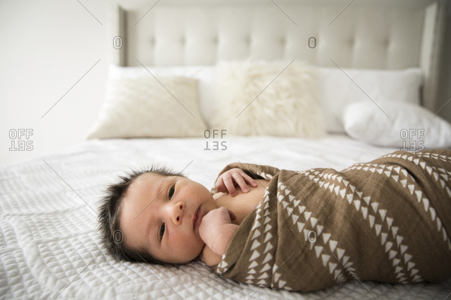 Newborn Baby With Lots of Dark Hair Lays Swaddled on Bed at Home