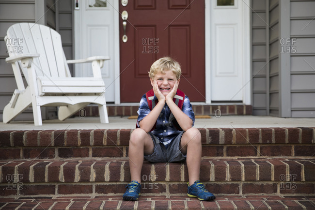 Smiling Blonde Boy Sits on Brick Front Steps With Head in Hands