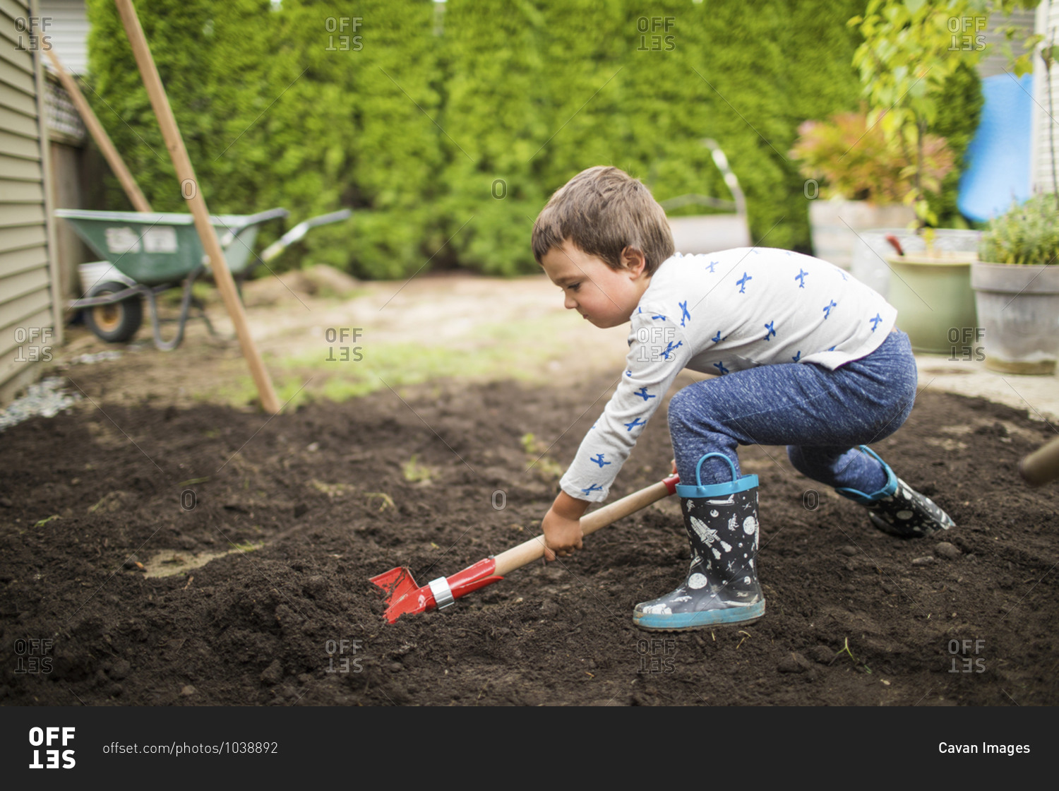 Young boy shoveling dirt, helping dad with landscape project.