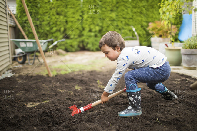 Young boy shoveling dirt helping dad with landscape project