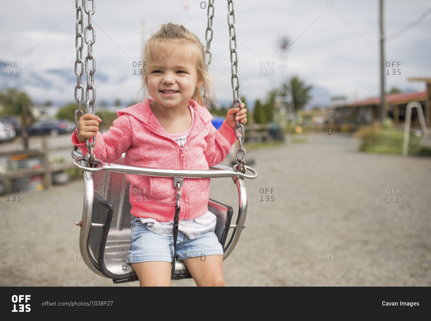 Cute young girl sitting on metal swing outside.