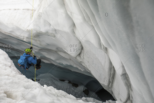 Mountaineer rappels into glacier crevasse to explore a cave.