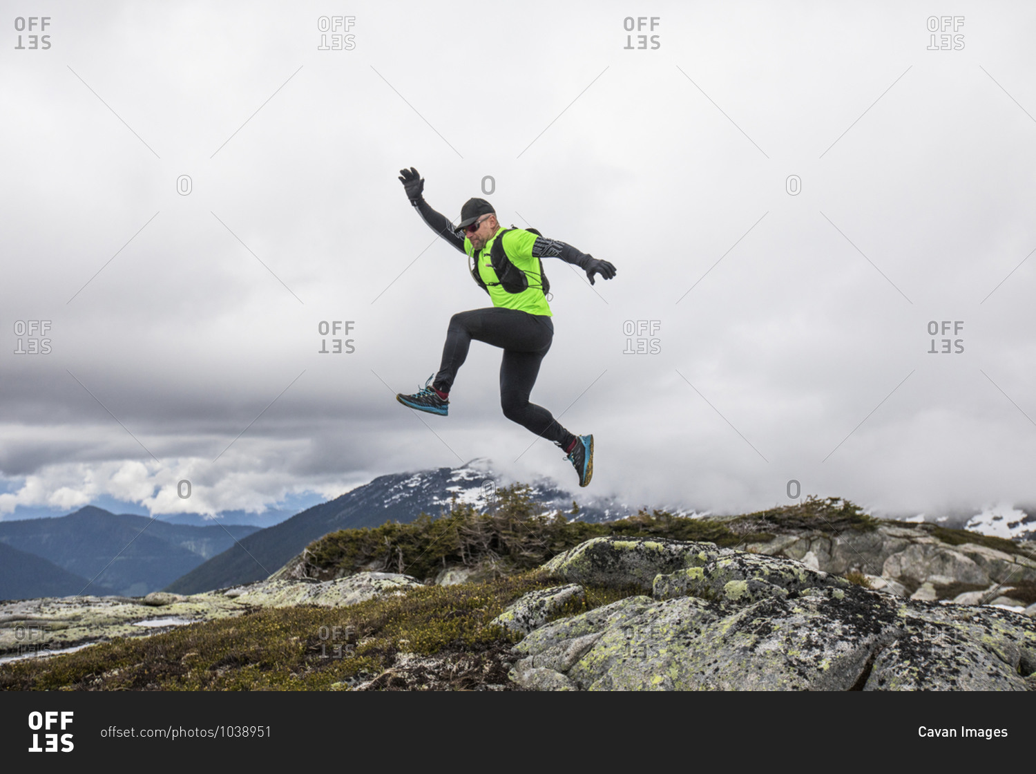 Trail runner jumps off rocks on mountain ridge.