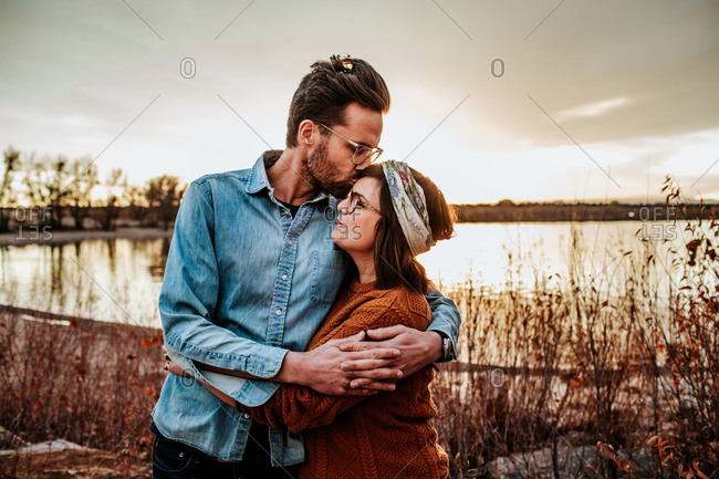 Hipster husband kissing smiling wife near a lake in Colorado