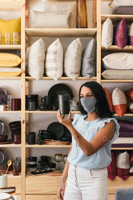 Woman with mask on looking at black ceramic cup in fancy home store