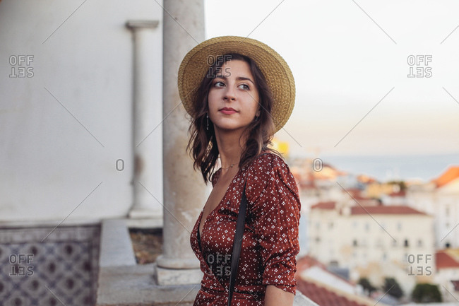 Woman in a straw hat looking aside and smiling, Lisbon sunset view