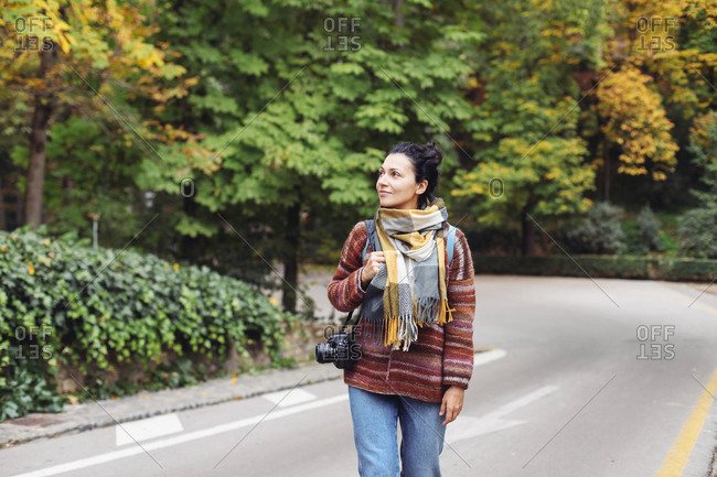 Woman in a sweater and scarf with a camera walking in a autumn forest