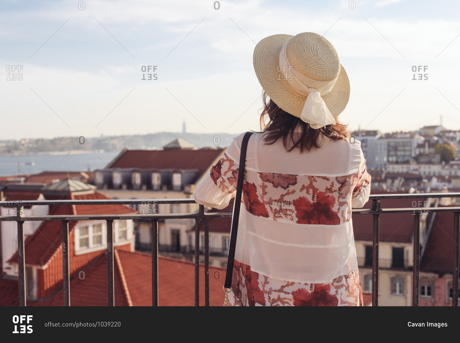 Woman in a straw hat from the back looking over red roofs on Lisbon