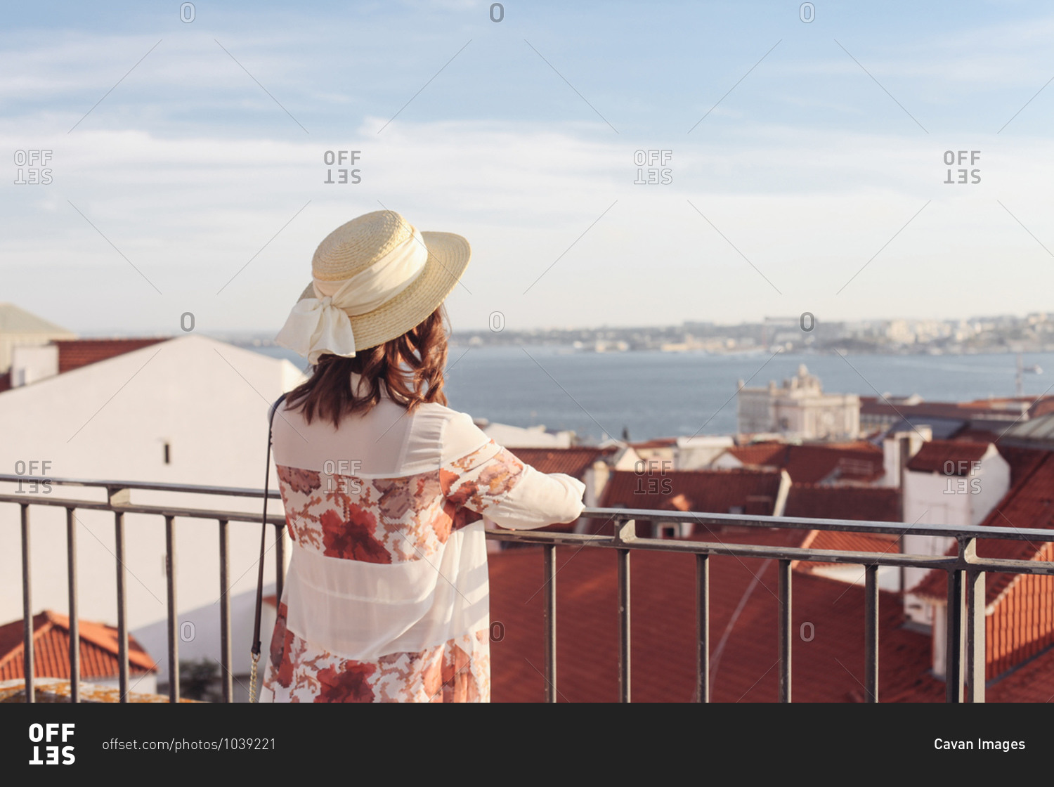 Woman in hat from the back looking over red roofs on Lisbon