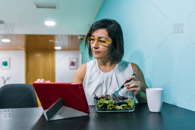 A woman using a tablet while eating healthy food
