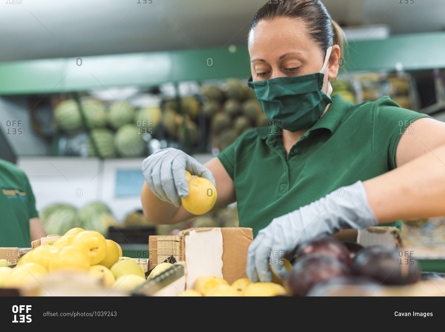 A woman wearing a mask placing fruit in the fruit shop