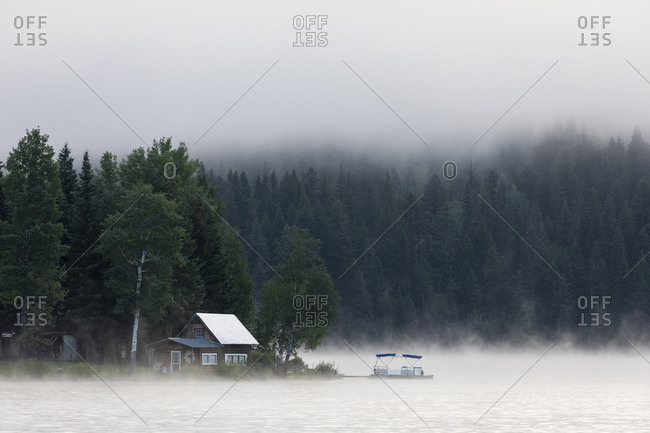 Canada, British Columbia - August 4, 2020: Wooden cabin on lake shore on foggy morning in British Columbia