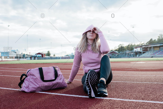Woman sits on a running track looking tired and thinking
