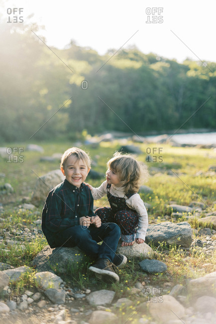 Two siblings whispering secrets to each other by the lake