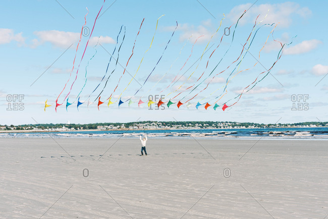 A boy chasing a large kite flying past him on a New England beach