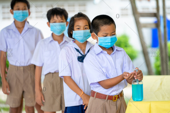 Elementary school students wearing hygienic mask and using hand sanitizer
