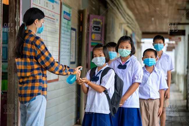 Teacher and elementary children with face mask are disinfecting their hands