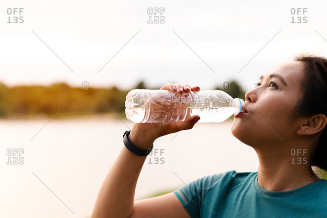 Athletic Asian woman drinking water after running