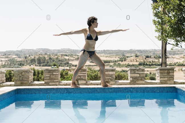 Woman in a swimsuit doing yoga at the edge of an outdoor pool
