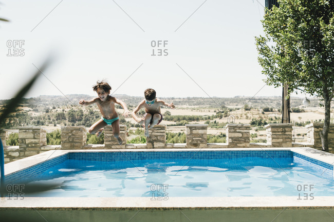 Boy and girl in swimsuit jumping into an outdoor pool in summer