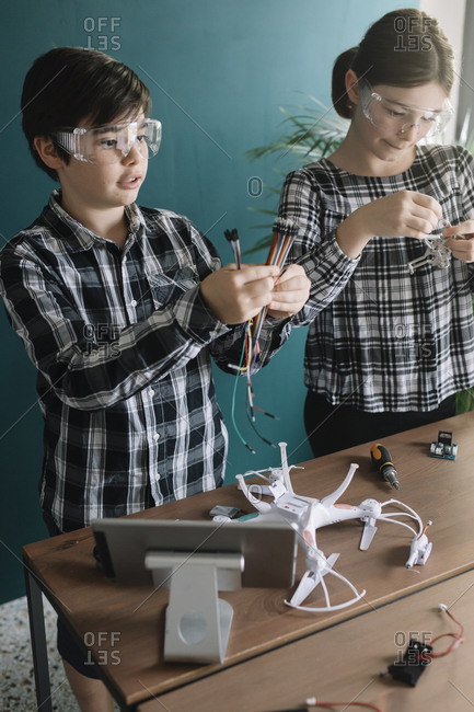 Siblings preparing drone on table while standing at home