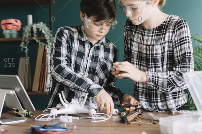 Siblings making quadcopter on table while standing at home