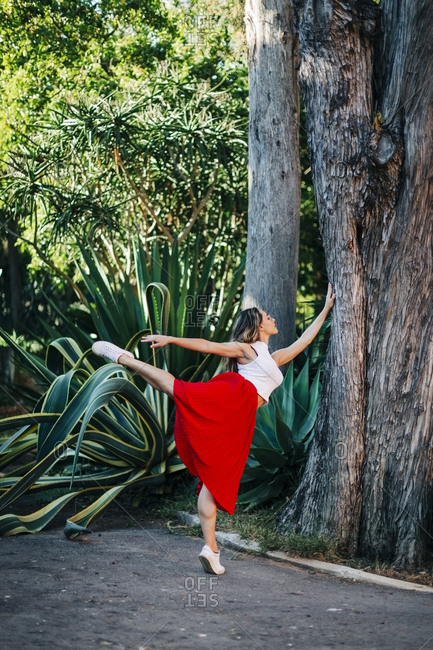 Young woman dancing ballet on footpath by tree trunk in park