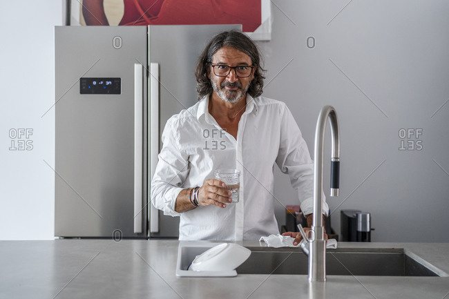 Smiling man drinking water while standing by sink in kitchen