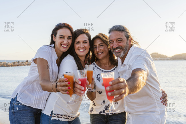 Smiling family holding drinks while standing against sea during sunset