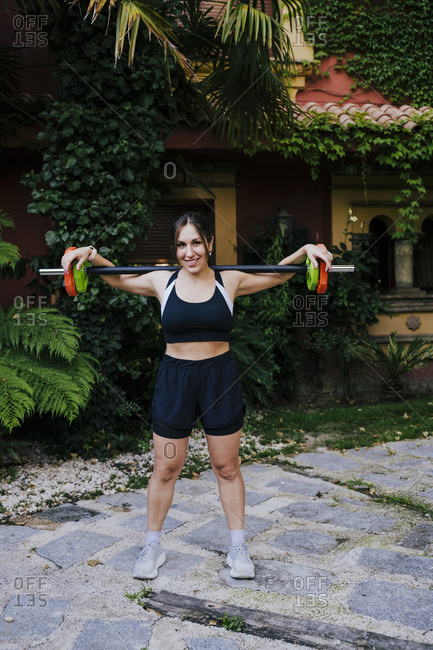 Smiling mid adult woman lifting weights while standing in yard