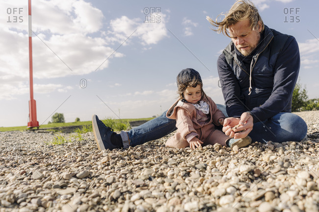 Father and daughter playing with pebbles on sunny day