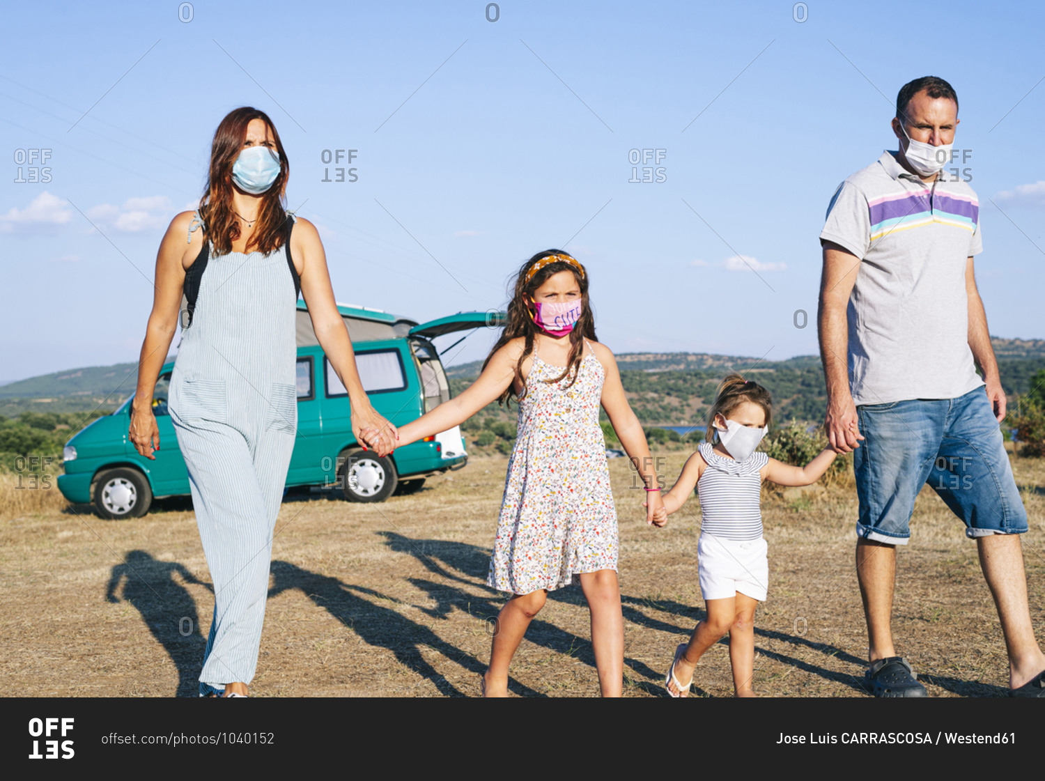 Family wearing masks holding hands while walking on landscape against sky