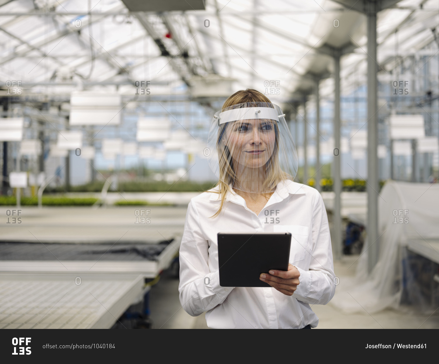 Businesswoman wearing face shield with digital tablet working in plant nursery