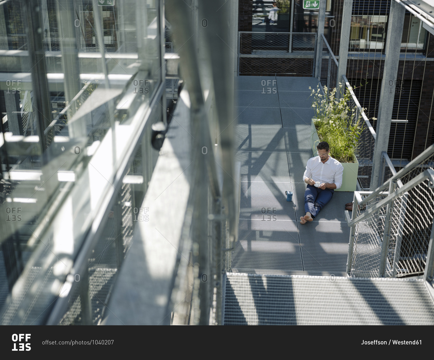 Businessman with coffee sitting on floor in greenhouse