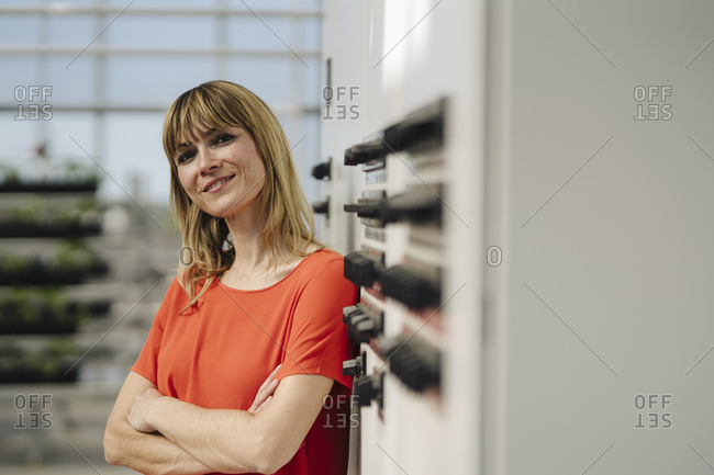 Smiling businesswoman with arms crossed standing by control panel in greenhouse
