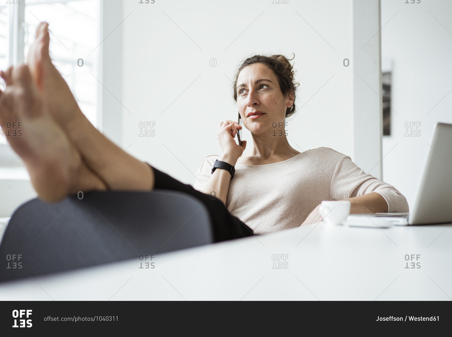 Businesswoman with feet on table talking over smart phone while relaxing