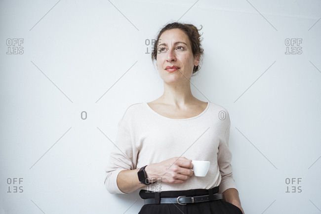 Thoughtful businesswoman holding coffee cup standing against white wall