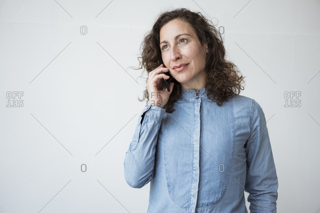 Businesswoman talking over mobile phone while standing against white wall